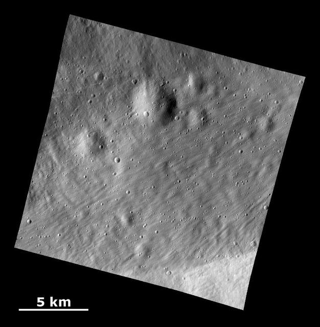 This image from NASA Dawn spacecraft shows a surface with craters buried under thick ejected material that displays a grooved texture on the giant asteroid Vesta.