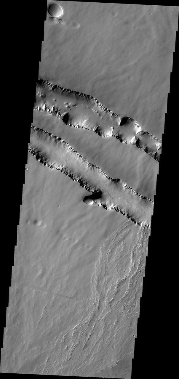 The two depression crossing this image are called Pavonis Fossae and are located just north of the volcano in this image captured by NASA 2001 Mars Odyssey spacecraft.