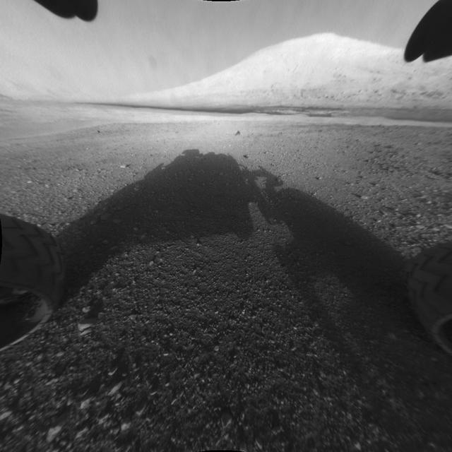 This image taken by NASA Curiosity shows what lies ahead for the rover -- its main science target, informally called Mount Sharp. The rover shadow can be seen in the foreground, and the dark bands beyond are dunes.