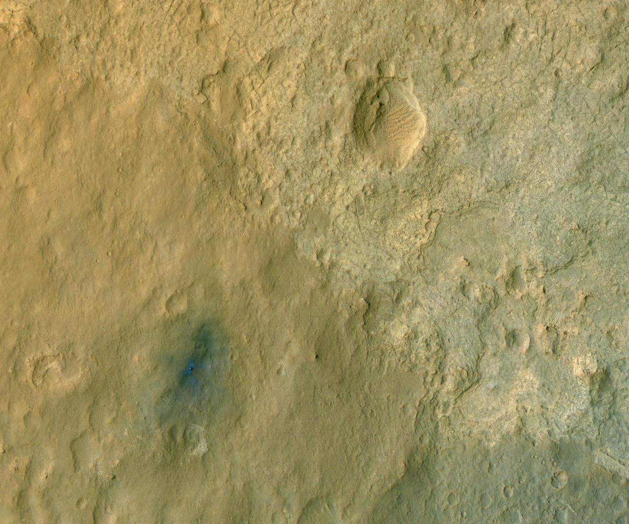 This color-enhanced view of NASA Curiosity rover on the surface of Mars was taken by NASA Mars Reconnaissance Orbiter as the satellite flew overhead. The descent stage blast pattern around the rover is clearly seen as relatively blue colors.