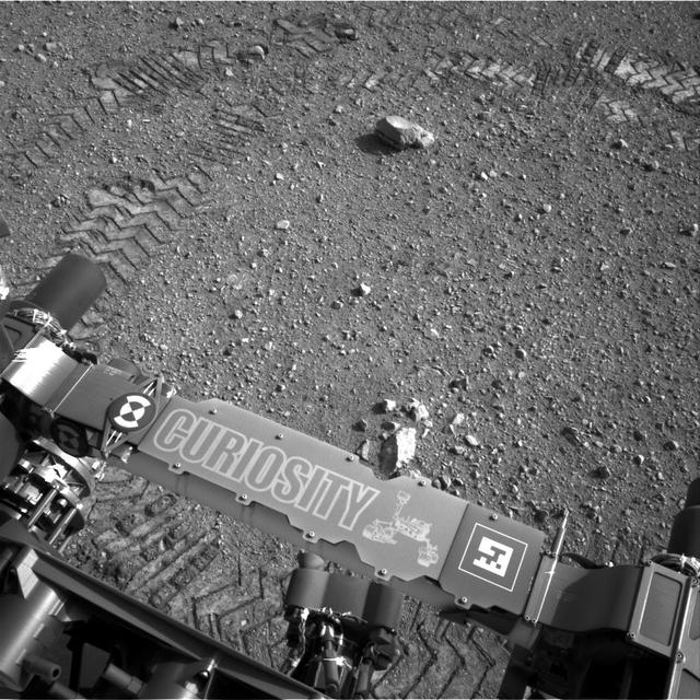 This image shows a close-up of track marks from the first test drive of NASA Curiosity rover. The rover arm is visible in the foreground. A close inspection of the tracks reveals a unique, repeating pattern: Morse code for JPL.