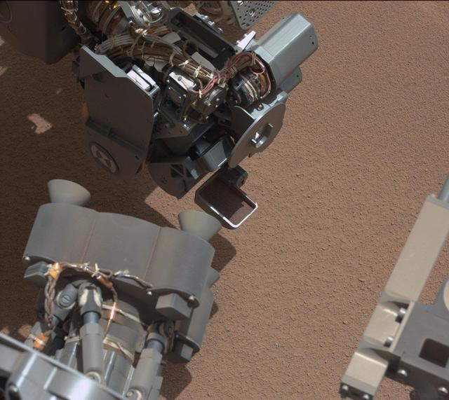 This image from NASA Curiosity shows a scoop full of sand and dust lifted by the rover first use of the scoop on its robotic arm. In the foreground, near bottom of this image, the bright object visible on the ground might be a piece of rover hardware.