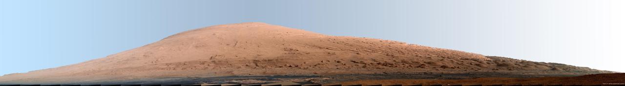 This mosaic of images from the Mast Camera Mastcam on NASA Mars rover Curiosity shows Mount Sharp in a white-balanced color adjustment that makes the sky look overly blue but shows the terrain as if under Earth-like lighting.
