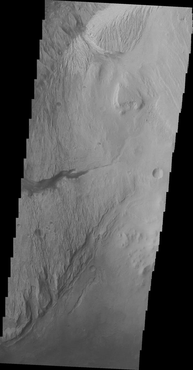 The highest elevations of Mt. Sharp are just outside this image to the east. In the center of this image from NASA Mars Odyssey spacecraft is a channel, indicating that fluids played a part in eroding Mt. Sharp.