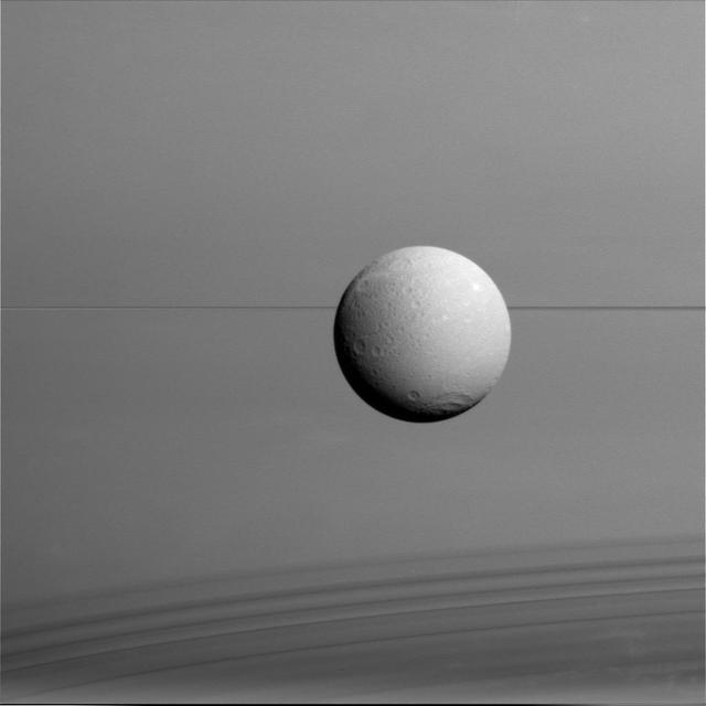 Dione hangs in front of Saturn and its icy rings in this view, captured during Cassini final close flyby of the icy moon. North on Dione is up.