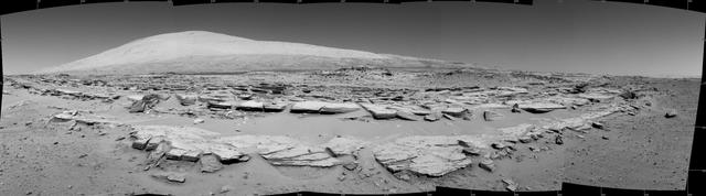 A landscape scene from NASA Curiosity Mars rover shows rock rows at Junda forming striations in the foreground, with Mount Sharp on the horizon.