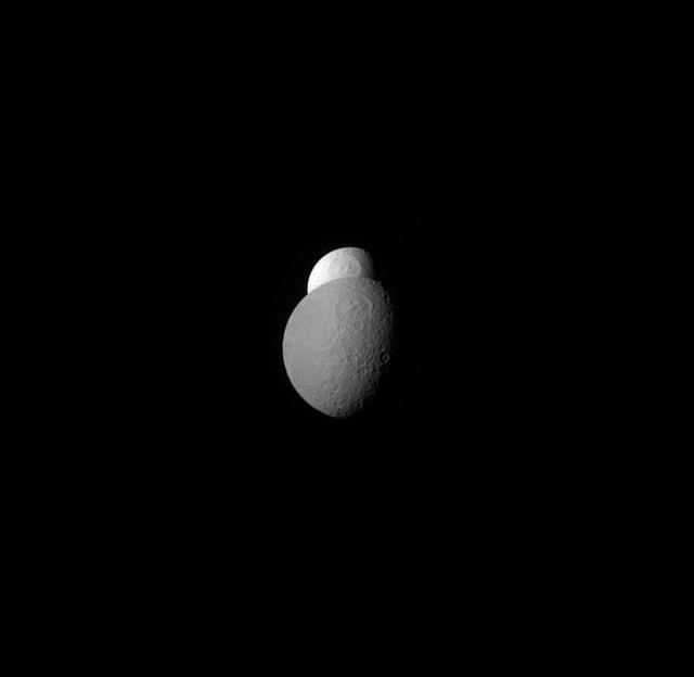 Tethys appears to be peeking out from behind Rhea, watching the watcher.  Scientists believe that Tethys' surprisingly high albedo is due to the water ice jets emerging from its neighbor, Enceladus. The fresh water ice becomes the E ring and can eventually arrive at Tethys, giving it a fresh surface layer of clean ice.  Lit terrain seen here is on the anti-Saturn side of Rhea. North on Rhea is up. The image was taken in red light with the Cassini spacecraft narrow-angle camera on April 20, 2012.  The view was obtained at a distance of approximately 1.1 million miles (1.8 million kilometers) from Rhea and at a Sun-Rhea-spacecraft, or phase, angle of 59 degrees. Image scale is 7 miles (11 kilometers) per pixel.  http://photojournal.jpl.nasa.gov/catalog/PIA18293