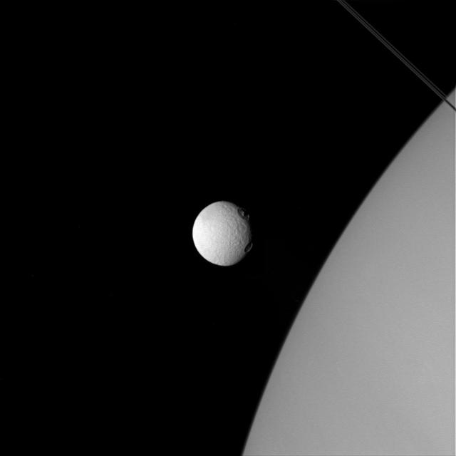 The two large craters on Tethys, near the line where day fades to night, almost resemble two giant eyes observing Saturn.  The location of these craters on Tethys' terminator throws their topography into sharp relief. Both are large craters, but the larger and southernmost of the two shows a more complex structure. The angle of the lighting highlights a central peak in this crater. Central peaks are the result of the surface reacting to the violent post-impact excavation of the crater. The northern crater does not show a similar feature. Possibly the impact was too small to form a central peak, or the composition of the material in the immediate vicinity couldn't support the formation of a central peak.  In this image Tethys is significantly closer to the camera, while the planet is in the background. Yet the moon is still utterly dwarfed by the giant Saturn.  This view looks toward the anti-Saturn side of Tethys. North on Tethys is up and rotated 42 degrees to the right. The image was taken in visible light with the Cassini spacecraft wide-angle camera on April 11, 2015.  The view was obtained at a distance of approximately 75,000 miles (120,000 kilometers) from Tethys. Image scale at Tethys is 4 miles (7 kilometers) per pixel.  http://photojournal.jpl.nasa.gov/catalog/pia18318