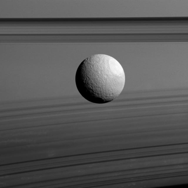 Saturn moon Tethys appears to float between two sets of rings in this view from NASA Cassini spacecraft, but it just a trick of geometry. The rings, which are seen nearly edge-on, are the dark bands above Tethys.
