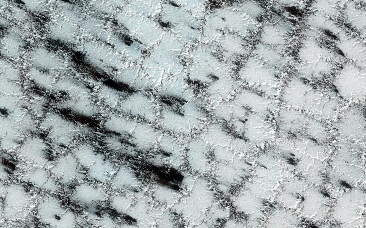 Although the season is late spring, carbon dioxide ice still covers much of the surface at this high latitude site. It is still a chilly -128 degrees Celsius. The weak boundaries of the polygonal structure of the surface have been eroded by spring sublimation of carbon dioxide as energy from the Sun turns ice to gas. The larger troughs in this image accentuate the surface polygonal structure, while the narrow cracks show the erosion caused when carbon dioxide gas escapes from under the seasonal ice layer carrying fine material from the surface. The dark fans in this image are made up of small particles from the surface deposited on top of the seasonal layer of ice. The fans originate at a crack, a weak spot that allows the gas to escape. The material is deposited in a direction determined by the direction of the wind as the gas was escaping. http://photojournal.jpl.nasa.gov/catalog/PIA19292