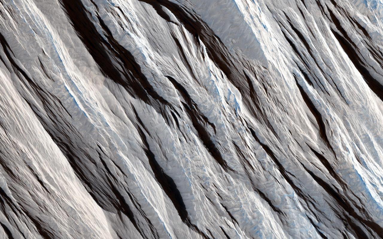 Some geological materials (like solid rock) are incredibly tough, but others (like piles of volcanic ash) are quite soft. Some materials are soft enough that they can be eroded by the wind alone and yield landscapes that look like what we see in this HiRISE image. The long straight ridges seen here are called yardangs and they form on Mars (and Earth) when the wind strips away the inter-ridge material. This process is greatly aided when the wind is also blowing sand along. The sand grains do an effective job at stripping away loose material: these ridges are literally being sandblasted. Yardangs are useful features to recognize because the tell us the direction the wind is blowing in. They take a long time to form so this direction is the dominant wind orientation averaged over a long period of time (which might be quite different that the winds on Mars today). These yardangs also tell us that the surface here is made up of loose weak material and this information, in conjunction with other data, can tell us what the material is composed of and what the history of this particular site on Mars has been. http://photojournal.jpl.nasa.gov/catalog/PIA19457