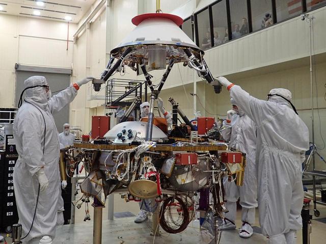 In this photo, spacecraft specialists at Lockheed Martin Space Systems, Denver, are reaching up to guide lowering of the parachute cone for installation onto NASA's InSight spacecraft. The photo was taken on April 29, 2015.  InSight's parachute, stowed inside the cone, will provide deceleration in the Martian atmosphere. Its role will come after atmospheric friction with the spacecraft's heat shield provides initial deceleration and before thrusters on the lander provide final deceleration.   InSight, for Interior Exploration Using Seismic Investigations, Geodesy and Heat Transport, is scheduled for launch in March 2016 and landing in September 2016. It will study the deep interior of Mars to advance understanding of the early history of all rocky planets, including Earth.  Note: After thorough examination, NASA managers have decided to suspend the planned March 2016 launch of the Interior Exploration using Seismic Investigations Geodesy and Heat Transport (InSight) mission. The decision follows unsuccessful attempts to repair a leak in a section of the prime instrument in the science payload.  http://photojournal.jpl.nasa.gov/catalog/PIA19669