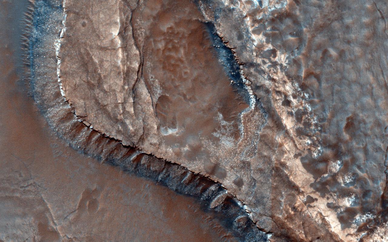 This image from NASA Mars Reconnaissance Orbiter shows the southwestern floor of a 50-kilometer diameter unnamed crater, about 100 kilometers northeast of Hellas Basin. The crater's rim is breached on both the north and south by a valley system that previously flowed across the crater floor, leaving behind an interesting array of channel patterns and deposits as it transported water and sediments into and out of the crater. In this image, we see a portion of the channel system along the southwestern crater floor near where the valley breaches the southern rim. The darker-toned surface has a pattern similar to the texture of a basketball, and blankets the region both in the channel belt and in the basin below the cliffs. Superposed on this patterned surface are clusters of larger, circular mounds that may be related to the thawing and freezing of ice-rich sediment, which is unusual at this relatively low latitude. Extensional cracks and clusters of pits make this topography more complicated. The southern part of this image reveals a prominent irregular scarp with light-toned layered deposits exposed along the margin beneath this textured surface. The light-toned layers look like an ancient mosaic in some areas as they are irregularly fractured and brecciated. Individual blocks and large boulders of this material are visible at full-resolution near the scarp, just about to fall and already lying on the debris slopes below the scarp. Some are brighter than the others: these may be dust-free, indicating that they have detached from the cliff more recently. http://photojournal.jpl.nasa.gov/catalog/PIA19850