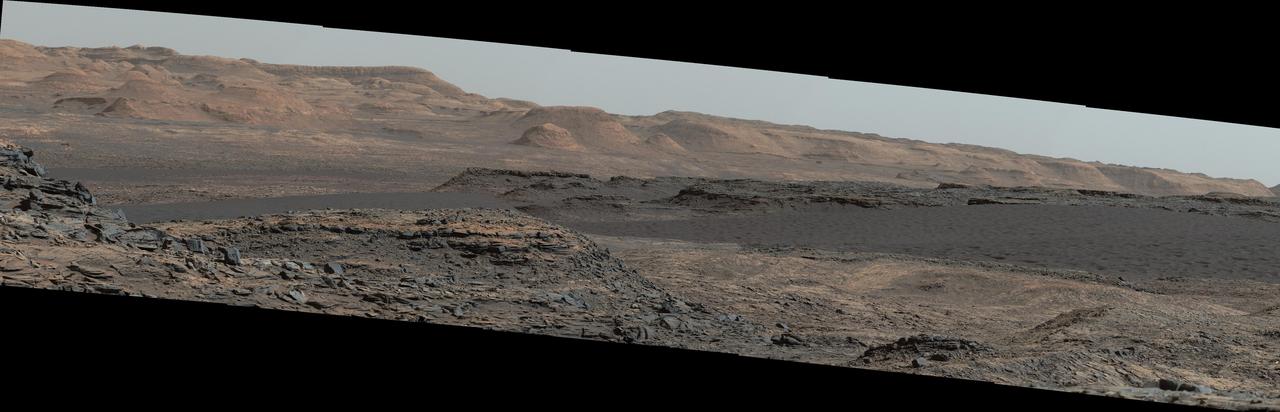 This view from the Mast Camera (Mastcam) on NASA's Curiosity Mars rover shows a dark sand dune in the middle distance. The rover's examination of dunes on the way toward higher layers of Mount Sharp will be the first in-place study of an active sand dune anywhere other than Earth.  The scene combines several images taken on Sept. 25, 2015, during the 1,115th Martian day, or sol, of Curiosity's work on Mars. The images are from Mastcam's right-eye camera, which has a telephoto lens. The view is toward south-southwest.  The dunes on Curiosity's route are part of a band of dunes called "Bagnold Dunes," along the northwestern edge of Mount Sharp. The informal naming recognizes British military engineer Ralph Bagnold (1896-1990), a pioneer in the study of how winds move sand particles of dunes on Earth. The dune field is evident as a dark band in orbital images of the area inside Gale Crater were Curiosity has been active since landing in 2012, such as a traverse map at PIA20162.  Dunes are larger than wind-blown ripples of sand or dust that Curiosity and other rovers have visited previously. One dune that Curiosity will investigate in coming days is as tall as a two-story building and as broad as a football field. Ripples on the surface of these Martian dunes are larger than ripples on the surfaces of sand dunes on Earth.  The scene is presented with a color adjustment that approximates white balancing, to resemble how the rocks and sand would appear under daytime lighting conditions on Earth.   http://photojournal.jpl.nasa.gov/catalog/PIA19928