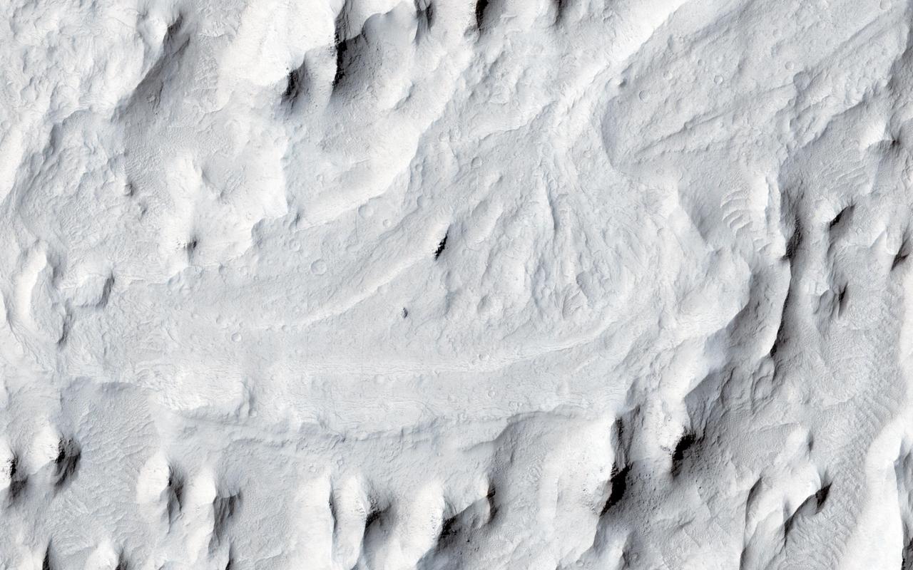 In this image from NASA Mars Reconnaissance Orbiter spacecraft, an ancient sinuous meandering river system is surrounded by features called yardangs. The yardangs are the ridge-like landforms that align approximately north-south. These features were created as the wind scoured and eroded the bedrock. The raised relief of the meandering river suggests inverted topography, likely due to lithification and cementation of the riverbed sediment. The cemented channel deposits were resistant, and thus less susceptible to erosion over time. However, the area surrounding the riverbed suggests that this area was a floodplain of weaker lithology that was subsequently eroded and shaped to the yardangs. The main meandering inverted riverbed within the image has a length of about 13 kilometers. The elevation of the channel at the top of the image is on the order of 113 meters higher than the bottom, based on Mars Orbiter Laser Altimeter (MOLA) data. This elevation difference and the increase in sinuosity of the channel shape in the southerly direction implies that the flow of the ancient river may have been heading south-southwest. http://photojournal.jpl.nasa.gov/catalog/PIA20047