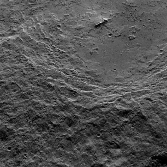 This view shows the southwestern rim of 106-mile-wide (170-kilometer-wide) Urvara crater on Ceres. The crater's terraced rim leads down to a generally smooth floor. In the crater's center is a prominent double peak, surrounded by rough terrain to the west and some linear, parallel grooves to the east. NASA's Dawn spacecraft obtained the image on Oct. 15, 2015, from an altitude of 915 miles (1,470 kilometers). It has a resolution of 450 feet (140 meters) per pixel. North on Ceres is up. http://photojournal.jpl.nasa.gov/catalog/PIA20134