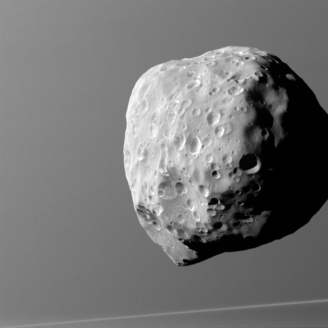 Epimetheus, seen here by NASA Cassini spacecraft, with Saturn in the background, is lumpy and misshapen, thanks in part to its size and formation process. Bombardment over the eons has left this tiny moon surface heavily pitted.