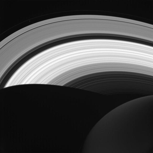 NASA's Cassini spacecraft looks down at the rings of Saturn from above the planet's nightside. The darkened globe of Saturn is seen here at lower right, along with the shadow it casts across the rings.  The image shows that even on the planet's night side, the rings remain in sunlight, apart from the portion that lies within Saturn's shadow. The rings also reflect sunlight back onto the night side of the planet, making it appear brighter than it would otherwise appear.  Saturn's small moon Prometheus (53 miles or 86 kilometers across) is faintly visible as a speck near upper left. The shadow of Saturn was once long enough to stretch to the orbit of Prometheus. But as northern summer solstice approaches, Saturn's shadow no longer reaches that far (see PIA20498). So Prometheus will not move into the darkness of the planet's shadow until the march of the seasons again causes the shadow to lengthen.  This view looks toward the sunlit side of the rings from about 41 degrees above the ring plane. The image was taken in visible light with the Cassini spacecraft wide-angle camera on Aug. 14, 2016.  The view was obtained at a distance of approximately 870,000 miles (1.4 million kilometers) from Saturn and at a Sun-Saturn-spacecraft, or phase, angle of 87 degrees. Image scale is 53 miles (86 kilometers) per pixel. Prometheus has been brightened by a factor of two to enhance its visibility.  http://photojournal.jpl.nasa.gov/catalog/PIA20505