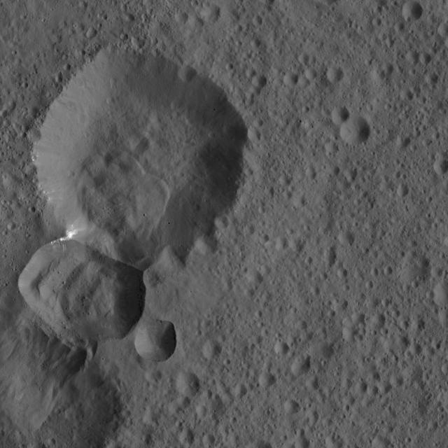 Two adjoining craters on Ceres are featured in this image from NASA Dawn spacecraft. A lobe-shaped feature is prominent in the larger crater interior. Bright material is visible at the intersection of the two craters.