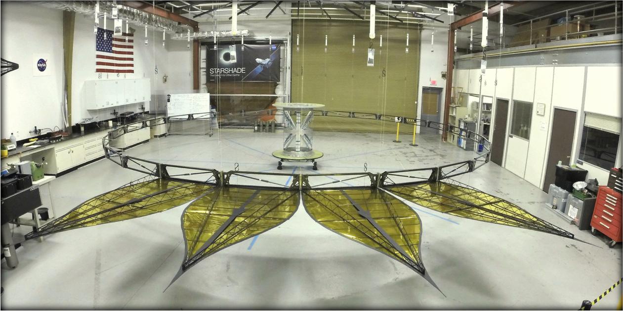 is image shows a deployed half-scale starshade with four petals at NASA's Jet Propulsion Laboratory, Pasadena, California in 2014. The full-scale of this starshade (not shown) will measure at 111 feet (34 meters). The flower-like petals of the starshade are designed to diffract bright starlight away from telescopes seeking the dim light of exoplanets. The starshade was re-designed from earlier models to allow these petals to furl, or wrap around the spacecraft, for launch into space. Each petal is covered in a high-performance plastic film that resembles gold foil.  On a starshade ready for launch, the thermal gold foil will only cover the side of the petals facing away from the telescope, with black on the other, so as not to reflect other light sources such as the Earth into its lens. The starshade is light enough for space and cannot support its own weight on Earth. Is it shown offloaded with counterweights, much like an elevator.  Starlight-blocking technologies such as the starshade are being developed to help image exoplanets, with a focus on Earth-sized, habitable worlds.  http://photojournal.jpl.nasa.gov/catalog/PIA20909