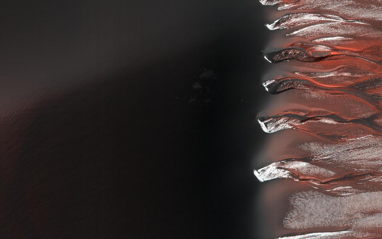 Kaiser Crater hosts a large field of sand dunes. Every winter the dunes are covered with a layer of seasonal carbon dioxide ice (dry ice). In early spring the ice begins to sublimate (going directly from solid ice to gas). In this image, the dunes are partially free of seasonal ice, with the contrast making it easy to see the ripples. Deep alcoves have been carved at the crest of the dune. We hypothesize that this is the result of the gas coming from the dry ice, destabilizing the sand at the crest. As blocks of ice protected in the cold shadows of the alcove break off they slide downslope, carving the channels we see. http://photojournal.jpl.nasa.gov/catalog/PIA21038