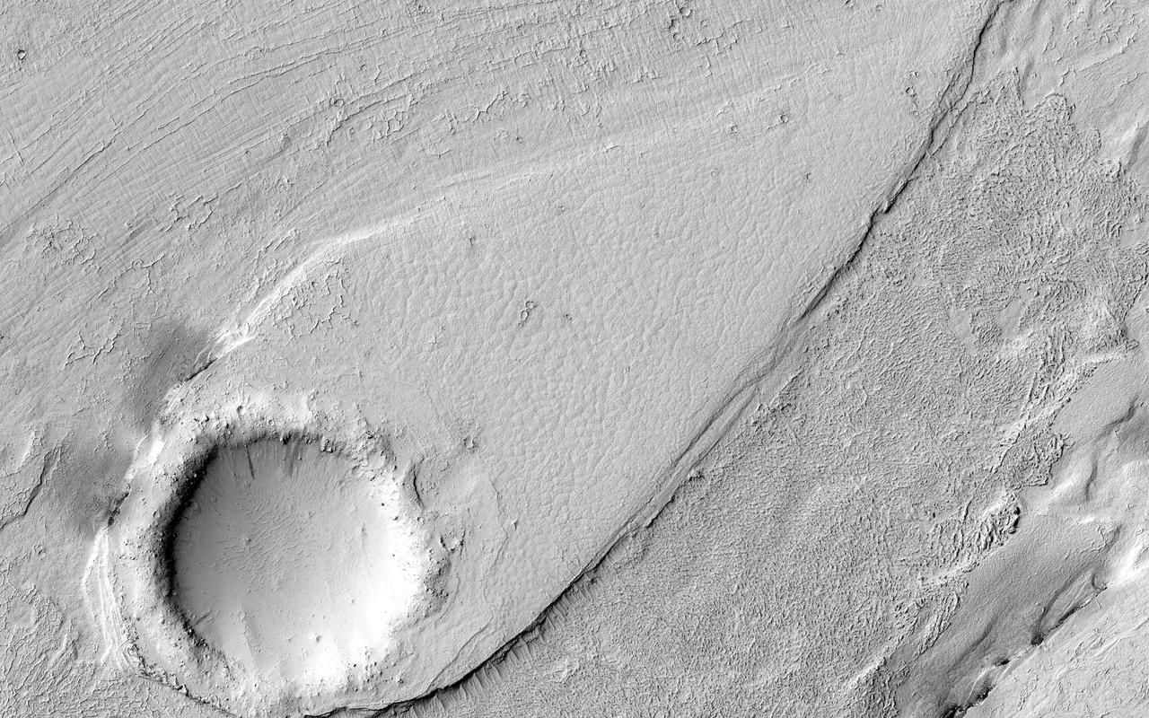 This image shows a portion of Lethe Vallis, an outflow channel that also transported lava. Another investigation of this area (Balme et al., 2011) discovered a repeat pattern of dune-like forms in the channel interpreted as fluvial dunes (or, giant current ripples) which are dunes formed by flowing water. This is one of only a few places on Mars where these pristine-appearing landforms have been identified. The channel formed by catastrophic floods, during which it produced the prominent crater-cored, teardroped-shaped island in the middle. The island has the blunter end pointing upstream and the long tail pointing downstream. Both the island and the fluvial dunes were formed by these extreme floods and their size is an indicator of the enormous discharges required to create them. The margins of the channel also show the terminal front of a pristine lava flow unit that inundated the channel from the south and the dunes show the remnants of another older lava flow. The top of the island displays polygonal patterned ground texture, which is a characteristic of periglacial processes in ice-rich ground. The dark materials from the channel and island walls are probably dark sand being eroded from an underlying horizontal basaltic (lava) layer. The crater at the core of the island has elongated dunes and reticulate dust ridges inside. This single image thus contains features formed by periglacial, volcanic, fluvial, impact, aeolian and mass wasting processes, all in one place. http://photojournal.jpl.nasa.gov/catalog/PIA21039