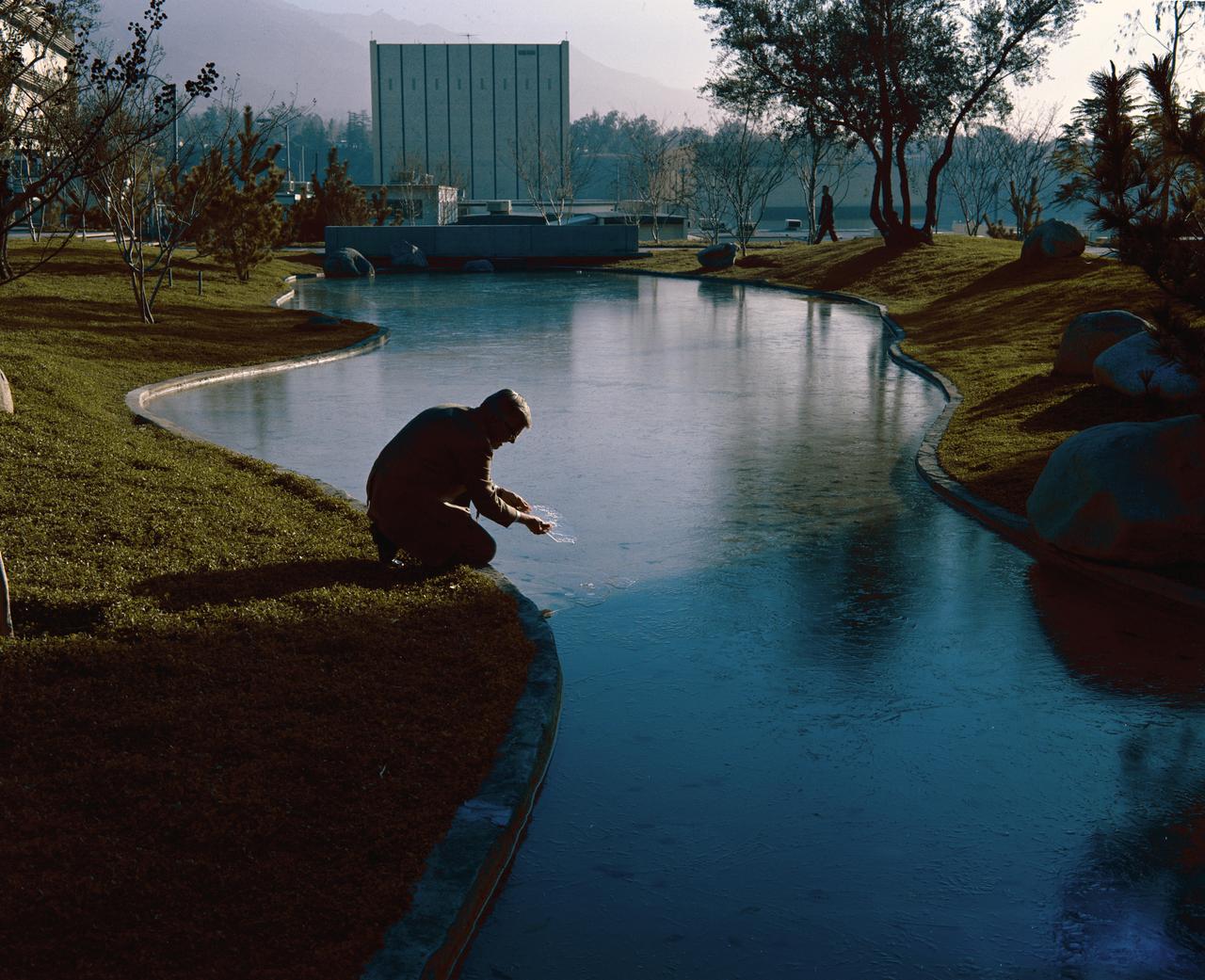 This archival image was released as part of a gallery comparing JPL's past and present, commemorating the 80th anniversary of NASA's Jet Propulsion Laboratory on Oct. 31, 2016.  This photograph from 1971 shows the open-air gathering area at NASA's Jet Propulsion Laboratory known as "The Mall." It looks east towards the Applied Mechanics building (the blocky white building now numbered 157). The person in the foreground is Robert Steinbacher, the project scientist for the Mariner 9 mission to Mars. The concrete bridge crossing the ponds remains, even though the ponds have been removed. Many trees and another building, the Central Engineering Building (301), block the view to Building 157 now.  http://photojournal.jpl.nasa.gov/catalog/PIA21125