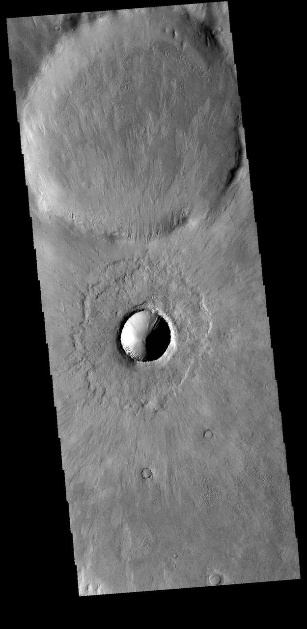 This image captured by NASA 2001 Mars Odyssey spacecraft shows two craters in Terra Cimmeria just north of Kepler Crater. The small crater in the middle of the image is a relatively new crater. The interior rim has gullies, but the bowl shape shows that there has been very little deposition of materials. Additionally, the radial emplacement of thin ejecta is still identifiable, and can be seen in the larger crater in the top of the image. With time the crater floor will flatten due to influx of materials and the subtle radial ejecta will be hidden by dust. While the actual age of the small crater is not known, it is relatively younger than the larger crater. Orbit Number: 66523 Latitude: -44.3019 Longitude: 139.301 Instrument: VIS Captured: 2016-12-12 09:31 http://photojournal.jpl.nasa.gov/catalog/PIA21300