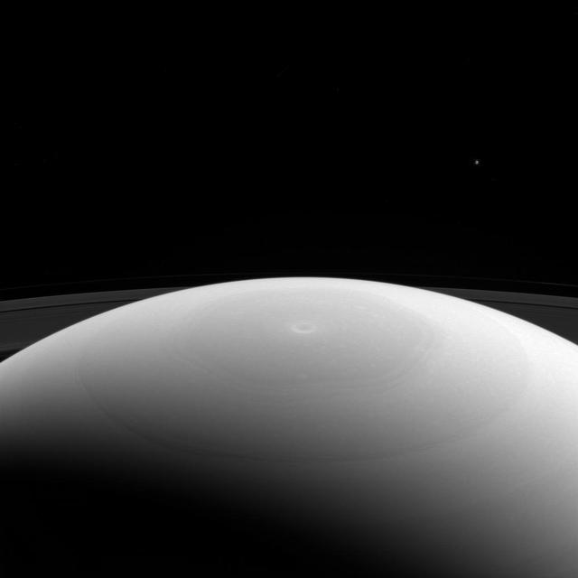 From high above Saturn's northern hemisphere, NASA's Cassini spacecraft gazes over the planet's north pole, with its intriguing hexagon and bullseye-like central vortex.  Saturn's moon Mimas is visible as a mere speck near upper right. At 246 miles (396 kilometers across) across, Mimas is considered a medium-sized moon. It is large enough for its own gravity to have made it round, but isn't one of the really large moons in our solar system, like Titan. Even enormous Titan is tiny beside the mighty gas giant Saturn.  This view looks toward Saturn from the sunlit side of the rings, from about 27 degrees above the ring plane. The image was taken in green light with the Cassini spacecraft wide-angle camera on March 27, 2017.  The view was acquired at a distance of approximately 617,000 miles (993,000 kilometers) from Saturn. Image scale is 37 miles (59 kilometers) per pixel. Mimas' brightness has been enhanced by a factor of 3 in this image to make it easier to see.  https://photojournal.jpl.nasa.gov/catalog/PIA21331