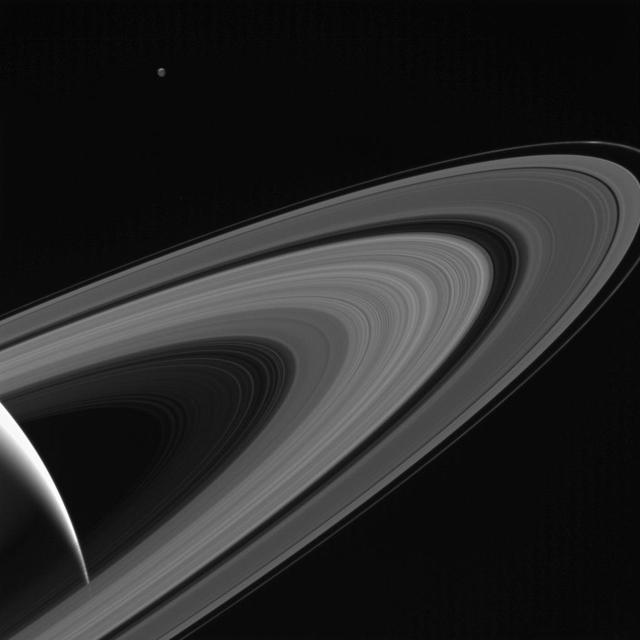 NASA's Cassini gazes across the icy rings of Saturn toward the icy moon Tethys, whose night side is illuminated by Saturnshine, or sunlight reflected by the planet.  Tethys was on the far side of Saturn with respect to Cassini here; an observer looking upward from the moon's surface toward Cassini would see Saturn's illuminated disk filling the sky.  Tethys was brightened by a factor of two in this image to increase its visibility. A sliver of the moon's sunlit northern hemisphere is seen at top. A bright wedge of Saturn's sunlit side is seen at lower left.  This view looks toward the sunlit side of the rings from about 10 degrees above the ring plane. The image was taken in visible light with the Cassini spacecraft wide-angle camera on May 13, 2017.  The view was acquired at a distance of approximately 750,000 miles (1.2 million kilometers) from Saturn and at a Sun-Saturn-spacecraft, or phase, angle of 140 degrees. Image scale is 43 miles (70 kilometers) per pixel on Saturn. The distance to Tethys was about 930,000 miles (1.5 million kilometers). The image scale on Tethys is about 56 miles (90 kilometers) per pixel.  https://photojournal.jpl.nasa.gov/catalog/PIA21342