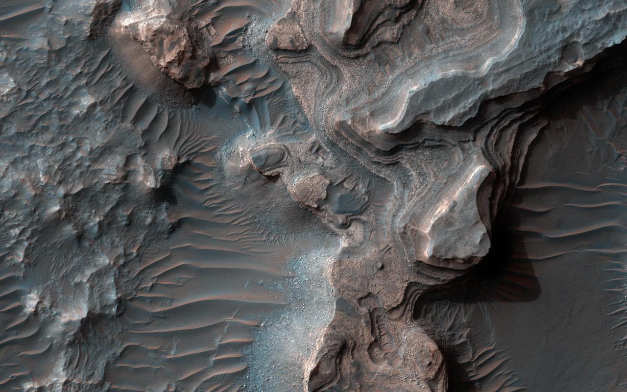 This image from NASA Mars Reconnaissance Orbiter shows layered deposits in Uzboi Vallis which sometimes occur in alcoves along the valley and/or below where tributaries enter into the lake from surrounding clay-bearing surfaces. http://photojournal.jpl.nasa.gov/catalog/PIA21563