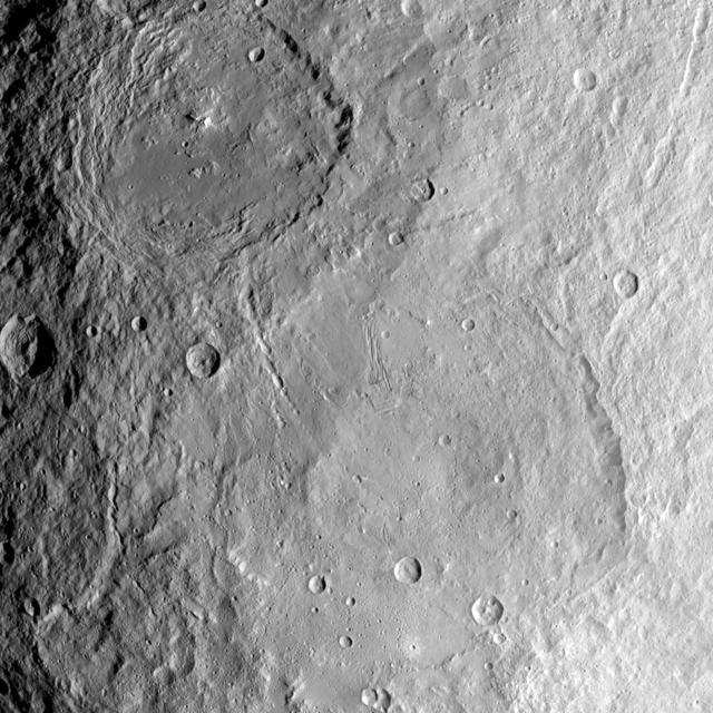 This image from NASA's Dawn spacecraft shows the large craters Urvara (top) and Yalode (bottom) on dwarf planet Ceres. These features are so big that they must be observed from high altitudes in order to fit in the frame of a single image. Urvara is (101 miles (163 kilometers) in diameter, while Yalode is 162 miles (260 kilometers) in diameter. The two giant craters were formed at different times. Yalode is almost 1 billion years older than Urvara, which is about 120 million to 140 million years old. Yalode's relatively smooth floor indicates Ceres' crust material became close to -- or even reached -- the melting temperature of ice as a consequence of the heat generated by the impact. On the other hand, the smaller Urvara has rougher terrain. This suggests Urvara had either a lower temperature increase from the impact, or a colder crust temperature at the time of the crater's formation, or a combination of the two. Indeed, Ceres' interior was warmer in the past, and has been slowly cooling as its supply of radioactive isotopes, whose decay represents Ceres' main heat source, has been decreasing over time. This picture also reveals geological details such, as the feature Nar Sulcus inside Yalode and a central peak in Urvara. Urvara is named after the Indian and Iranian deity of plants and fields. Yalode is named for the Dahomey goddess, worshipped by women at the harvest rites. This image was obtained by NASA's Dawn spacecraft on June 9, 2015. The spacecraft was then in its survey orbit (2,700 miles, 4,400 kilometers above the surface), when the footprint of Dawn's framing camera on Ceres' surface was about 260 miles (420 kilometers) across on Ceres' surface. The resolution is 1,400 feet (410 meters) per pixel. The central coordinates of the picture are 43 degrees south latitude, 278 degrees east in longitude. https://photojournal.jpl.nasa.gov/catalog/PIA21917
