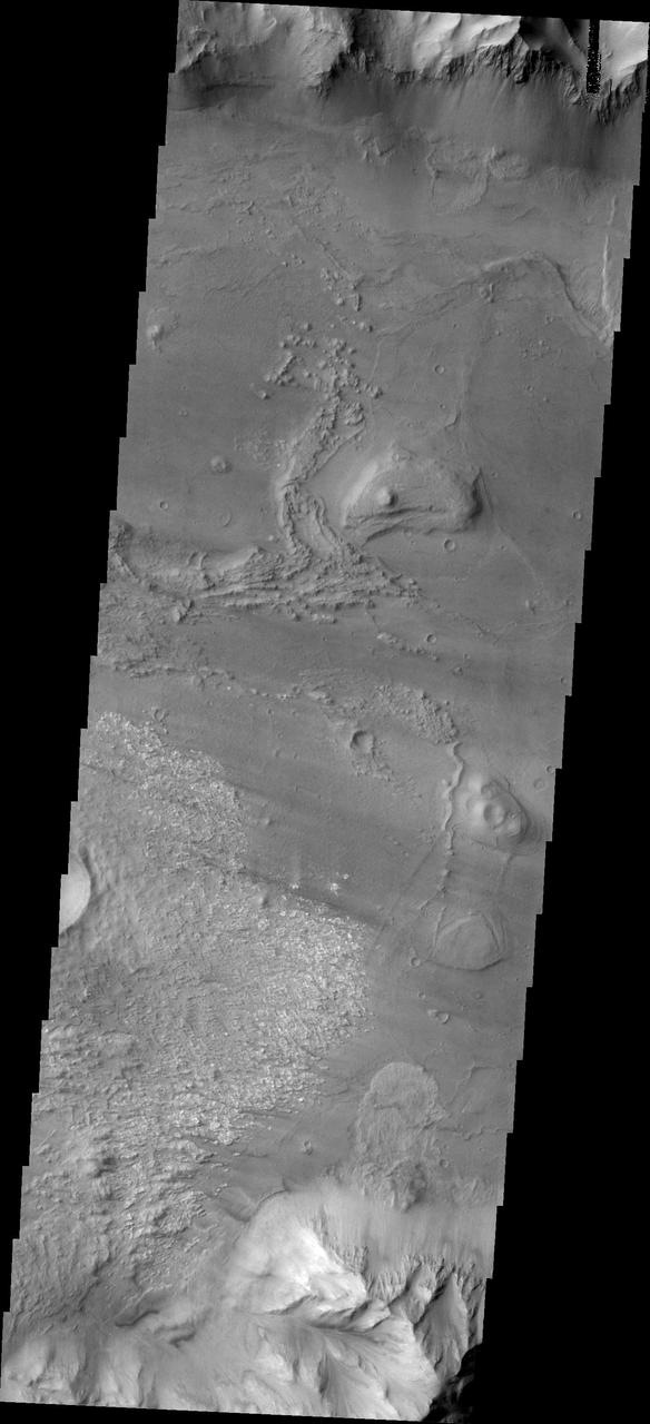 Coprates Chasma is one of the numerous canyons that make up Valles Marineris. The chasma stretches for 960 km (600 miles) from Melas Chasma to the west and Capri Chasma to the east. Landslide deposits, layered materials and sand dunes cover a large portion of the chasma floor. This image is located in central Coprates Chasma. In this image, there is a landslide deposit at the bottom of the image. The brighter material to the left of the landslide appears to be a rough surface likely etched by wind action. The chasma contains numerous regions of sand dunes, indicating that the wind plays a part in the erosion and deposition of fine materials in the canyon. The Odyssey spacecraft has spent over 15 years in orbit around Mars, circling the planet more than 69000 times. It holds the record for longest working spacecraft at Mars. THEMIS, the IR/VIS camera system, has collected data for the entire mission and provides images covering all seasons and lighting conditions. Over the years many features of interest have received repeated imaging, building up a suite of images covering the entire feature. From the deepest chasma to the tallest volcano, individual dunes inside craters and dune fields that encircle the north pole, channels carved by water and lava, and a variety of other feature, THEMIS has imaged them all. For the next several months the image of the day will focus on the Tharsis volcanoes, the various chasmata of Valles Marineris, and the major dunes fields. We hope you enjoy these images! Orbit Number: 35820 Latitude: -12.793 Longitude: 297.407 Instrument: VIS Captured: 2010-01-10 16:39 https://photojournal.jpl.nasa.gov/catalog/PIA21996