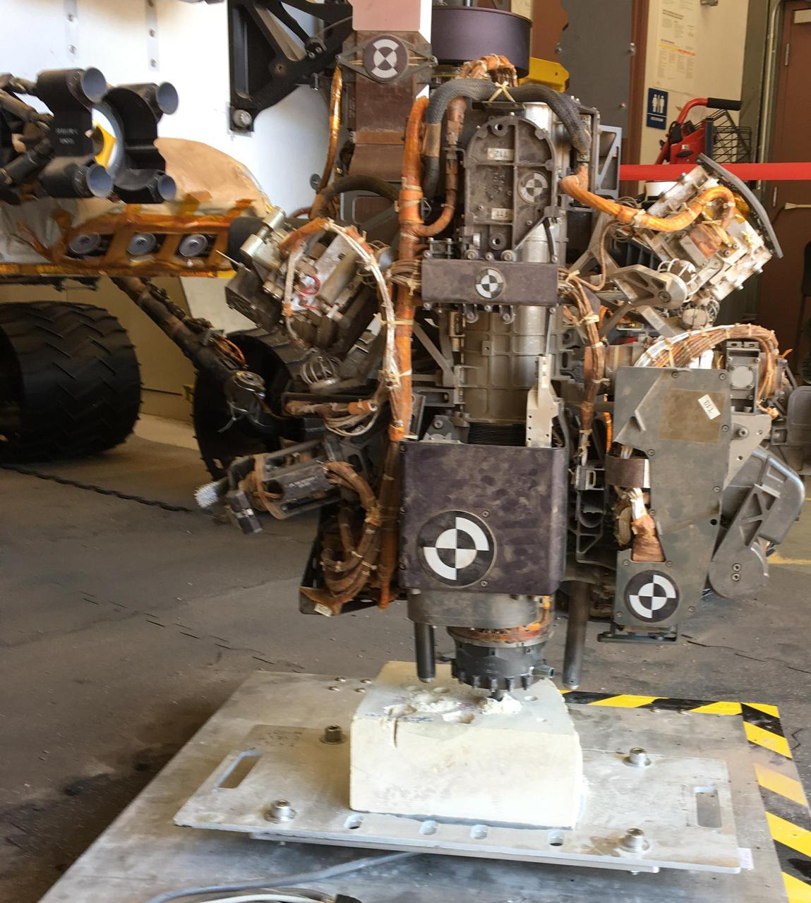 This photo taken in the "Mars Yard" at NASA's Jet Propulsion Laboratory, Pasadena, California, on Aug. 1, 2017, shows a step in development of possible alternative techniques that NASA's Curiosity Mars rover might be able to use to resume drilling into rocks on Mars.  In late 2016, after Curiosity's drill had collected sample material from 15 Martian rocks in four years, the drill's feed mechanism ceased working reliably. That motorized mechanism moved the bit forward or back with relation to stabilizer posts on either side of the bit. In normal drilling by Curiosity, the stabilizers were positioned on the target rock first, and then the feed mechanism extended the rotation-percussion bit into the rock.  In the alternative technique seen here, called "feed-extended drilling," the test rover's stabilizers are not used to touch the rock. The bit is advanced into the rock by motion of the robotic arm rather than the drill's feed mechanism.  https://photojournal.jpl.nasa.gov/catalog/PIA22062