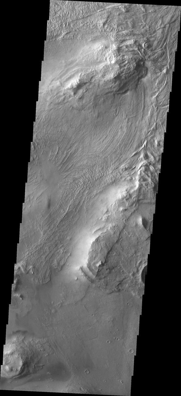 Melas Chasma is part of the largest canyon system on Mars, Valles Marineris. At only 563 km long (349 miles) it is not the longest canyon, but it is the widest. Located in the center of Valles Marineris, it has depths up to 9 km below the surrounding plains, and is the location of many large landslide deposits, as will as layered materials and sand dunes. There is evidence of both water and wind action as modes of formation for many of the interior deposits. Today's image covers part of the floor of the canyon. At the top of the image is one of the many hills found on the floor in this region. The linear grooved surface is part of a landslide deposit. Melas Chasma has many large landslide regions. Landslide deposits often have grooved surfaces with the grooves parallel to the direction of movement as the slide occurred. The ends of the landslide typically have a lobate edge, and will flow around large preexisting landforms.  The Odyssey spacecraft has spent over 15 years in orbit around Mars, circling the planet more than 69000 times. It holds the record for longest working spacecraft at Mars. THEMIS, the IR/VIS camera system, has collected data for the entire mission and provides images covering all seasons and lighting conditions. Over the years many features of interest have received repeated imaging, building up a suite of images covering the entire feature. From the deepest chasma to the tallest volcano, individual dunes inside craters and dune fields that encircle the north pole, channels carved by water and lava, and a variety of other feature, THEMIS has imaged them all. For the next several months the image of the day will focus on the Tharsis volcanoes, the various chasmata of Valles Marineris, and the major dunes fields. We hope you enjoy these images!  Orbit Number: 19112 Latitude: -11.1675 Longitude: 289.748 Instrument: VIS Captured: 2006-04-05 23:00  https://photojournal.jpl.nasa.gov/catalog/PIA22132