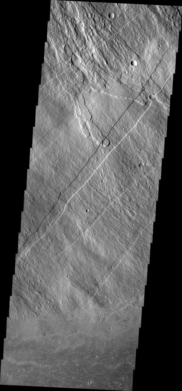 This image shows part of the southeastern flank of Arsia Mons, including the flat lying flows around the base of the volcano. These flows are located at the bottom of the image. Numerous small lava channels are visible aligned sub-parallel to the base of the volcano. Several narrow, lobate flows show the downslope direction from the top left of the image towards the bottom right. Running against this elevation change are large paired faults called graben. Graben form by faults that have allowed the material between them to "slide" down. The resultant topography is a linear depression. None of the lobate flows enter and then run along the fault valley, indicating that the faulting occurred after the lava flows.  Arsia Mons is the southernmost of the Tharsis volcanoes. It is 270 miles (450km) in diameter, almost 12 miles (20km) high, and the summit caldera is 72 miles (120km) wide. For comparison, the largest volcano on Earth is Mauna Loa. From its base on the sea floor, Mauna Loa measures only 6.3 miles high and 75 miles in diameter. A large volcanic crater known as a caldera is located at the summit of all of the Tharsis volcanoes. These calderas are produced by massive volcanic explosions and collapse. The Arsia Mons summit caldera is larger than many volcanoes on Earth.  The Odyssey spacecraft has spent over 15 years in orbit around Mars, circling the planet more than 69000 times. It holds the record for longest working spacecraft at Mars. THEMIS, the IR/VIS camera system, has collected data for the entire mission and provides images covering all seasons and lighting conditions. Over the years many features of interest have received repeated imaging, building up a suite of images covering the entire feature. From the deepest chasma to the tallest volcano, individual dunes inside craters and dune fields that encircle the north pole, channels carved by water and lava, and a variety of other feature, THEMIS has imaged them all. For the next several months the image of the day will focus on the Tharsis volcanoes, the various chasmata of Valles Marineris, and the major dunes fields. We hope you enjoy these images!  Orbit Number: 17691 Latitude: -11.2622 Longitude: 241 Instrument: VIS Captured: 2005-12-09 23:06  https://photojournal.jpl.nasa.gov/catalog/PIA22154