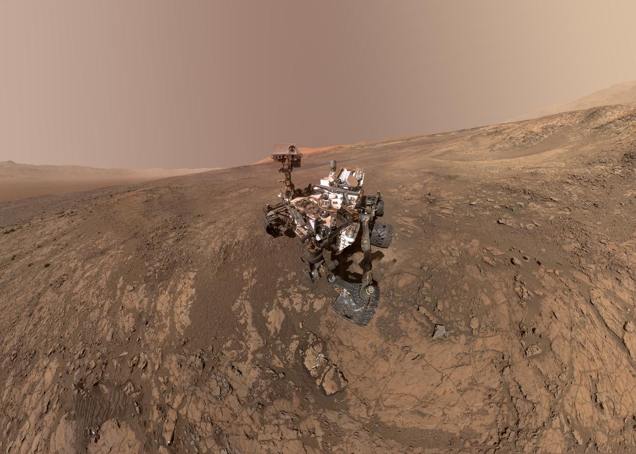 This self-portrait of NASA's Curiosity Mars rover shows the vehicle on Vera Rubin Ridge, which it's been investigating for the past several months. Directly behind the rover is the start of a clay-rich slope scientists are eager to begin exploring. In the coming week, Curiosity will begin to climb this slope. North is on the left and west is on the right, with Gale Crater's rim on the horizon of both edges.  Poking up just behind Curiosity's mast is Mount Sharp, photobombing the robot's selfie. Curiosity landed on Mars five years ago with the intention of studying lower Mount Sharp, where it will remain for all of its time on Mars. The mountain's base provides access to layers formed over millions of years. These layers formed in the presence of water -- likely due to a lake or lakes that sat at the bottom of the mountain, which sits inside of Gale Crater.  This mosaic was assembled from dozens of images taken by Curiosity's Mars Hands Lens Imager (MAHLI). They were all taken on Jan. 23, 2018, during Sol 1943.  The view does not include the rover's arm nor the MAHLI camera itself, except in the miniature scene reflected upside down in the parabolic mirror at the top of the mast. That mirror is part of Curiosity's Chemistry and Camera (ChemCam) instrument. MAHLI appears in the center of the mirror.  Wrist motions and turret rotations on the arm allowed MAHLI to acquire the mosaic's component images. The arm was positioned out of the shot in the images, or portions of images, that were used in this mosaic.  A full-resolution image is available at https://photojournal.jpl.nasa.gov/catalog/PIA22207
