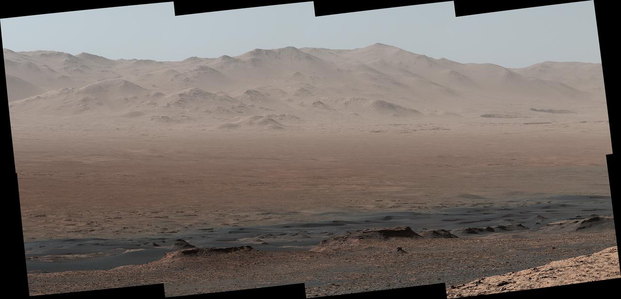 A vantage point on "Vera Rubin Ridge" provided NASA's Curiosity Mars rover this detailed look back over the area where it began its mission inside Gale Crater, plus more-distant features of the crater.  This view toward the north-northeast combines eight images taken by the right-eye, telephoto-lens camera of Curiosity's Mast Camera (Mastcam). It shows more detail of a fraction of the area pictured in a more sweeping panorama (see PIA22210) acquired from the same rover location using Mastcam's left-eye, wider-angle-lens camera. The scene has been white-balanced so the colors of the rock materials resemble how they would appear under daytime lighting conditions on Earth.  The component images were taken on Oct. 25, 2017, during the 1,856th Martian day, or sol, of the rover's work on Mars. At that point, Curiosity had gained 1,073 feet (327 meters) in elevation and driven 10.95 miles (17.63 kilometers) from its landing site.  Mount Sharp stands about 3 miles (5 kilometers) high in the middle of Gale Crater, which spans 96 miles (154 kilometers) in diameter. Vera Rubin Ridge is on the northwestern flank of lower Mount Sharp. The right foreground of this panorama shows a portion of Vera Rubin Ridge. In the distance is the northern wall of Gale Crater, with the rim crest forming the horizon roughly 25 miles (40 kilometers) from the rover's location.  An annotated version, Figure 1, indicates where the rover landed (at "Bradbury Landing") in 2012 and the initial portion of its drive, including investigation sites "Yellowknife Bay," "Darwin" and "Cooperstown." The rover's exact landing site is hidden behind a slight rise. The heat shield, back shell, and parachute used during the spacecraft's descent are within the pictured area but not recognizable due to the distance and to camouflaging by dust. At Yellowknife Bay in 2013, the mission found evidence of an ancient freshwater-lake environment that offered all of the basic chemical ingredients for microbial life.  Figure 2 includes three scale bars: of 40 meters (131 feet) at a distance of about 1,530 meters (1,673 yards) near the base of Mount Sharp; of 1,500 meters (1,640 yards) at a distance of about 30.75 kilometers (19.1 miles) near the base of the crater wall; and of 2,000 meters (1.2 miles) at a distance of about 41.2 kilometers (25.6 miles) at the crest of the rim.  Annotated images are available at https://photojournal.jpl.nasa.gov/catalog/PIA22209