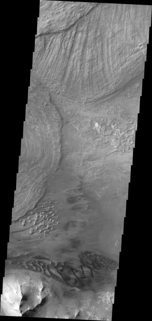 This VIS image shows the eastern end of Ius Chasma. The southern canyon wall is at the bottom of the image, with dark sand and sand dunes. The presence of mobile sand indicates that winds are eroding, depositing and changing the canyon floor. The rest of the image is dominated by large landslide deposits. At the top of the image are two overlapping deposits from landslides originating on the northern chasma wall. The landslide deposit on the left side of the image originate from the southern chasma wall. A landslide is a failure of slope due to gravity. They initiate due to several reasons. A lower layer of poorly cemented/resistant material may have been eroded, undermining the wall above which then collapses; earthquake seismic waves can cause the slope to collapse; and even an impact event near the canyon wall can cause collapse. As millions of tons of material fall and slide down slope a scalloped cavity forms at the upper part where the slope failure occurred. At the material speeds downhill it will pick up more of the underlying slope, increasing the volume of material entrained into the landslide. Whereas some landslides spread across the canyon floor forming lobate deposits, very large volume slope failures will completely fill the canyon floor in a large complex region of chaotic blocks. Ius Chasma is at the western end of Valles Marineris, south of Tithonium Chasma. Valles Marineris is over 4000 kilometers long, wider than the United States. Ius Chasma is almost 850 kilometers long (528 miles), 120 kilometers wide and over 8 kilometers deep. In comparison, the Grand Canyon in Arizona is about 175 kilometers long, 30 kilometers wide, and only 2 kilometers deep. The canyons of Valles Marineris were formed by extensive fracturing and pulling apart of the crust during the uplift of the vast Tharsis plateau. Landslides have enlarged the canyon walls and created deposits on the canyon floor. Weathering of the surface and influx of dust and sand have modified the canyon floor, both creating and modifying layered materials. There are many features that indicate flowing and standing water played a part in the chasma formation. The Odyssey spacecraft has spent over 15 years in orbit around Mars, circling the planet more than 71,000 times. It holds the record for longest working spacecraft at Mars. THEMIS, the IR/VIS camera system, has collected data for the entire mission and provides images covering all seasons and lighting conditions. Over the years many features of interest have received repeated imaging, building up a suite of images covering the entire feature. From the deepest chasma to the tallest volcano, individual dunes inside craters and dune fields that encircle the north pole, channels carved by water and lava, and a variety of other feature, THEMIS has imaged them all. For the next several months the image of the day will focus on the Tharsis volcanoes, the various chasmata of Valles Marineris, and the major dunes fields. We hope you enjoy these images! Orbit Number: 36744 Latitude: -8.64709 Longitude: 282.235 Instrument: VIS Captured: 2010-03-27 18:32 https://photojournal.jpl.nasa.gov/catalog/PIA22285