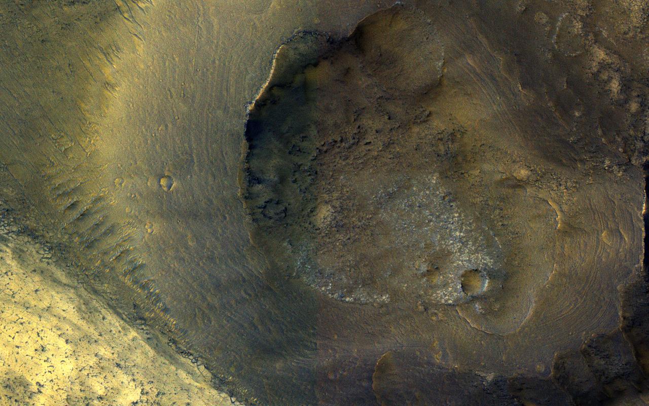 This image from NASA's Mars Reconnaissance Orbiter (MRO) shows a hill with a central crater. Such features have been interpreted as both mud volcanoes (really a sedimentary structure) and as actual volcanoes (the erupting lava kind). They occur on the floor of Valles Marineris below a closed topographic contour that could have held a lake, and the compaction of wet sediments may have created mud volcanoes. The fracture pattern of the bright flow unit surrounding the hill resembles mud cracks. However, there have also been observations from the CRISM instrument interpreted as high-temperature minerals, suggesting actual volcanism, although not necessarily at this location. Fine layers in the hill are consistent with either volcanism or mud flows. Either way, this activity is relatively recent in geologic time and may mark habitable subsurface environments. https://photojournal.jpl.nasa.gov/catalog/PIA22514