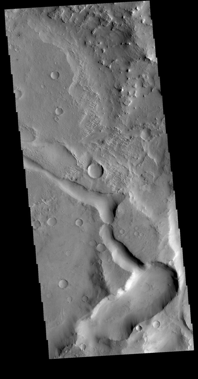 This VIS image is located in Terra Sabaea near the margin of Syrtis Major Planum. The channel-like feature in the bottom of the image is an unnamed feature. There is a high spot within the channel that would not let a fluid pass from one side to the other. This indicates that this is not a water carved channel, but was most likely an underground lava tube, where collapse of the roof has revealed the underlying feature. The 90 degree turns in the channel feature, and the small linear ridges just to the top of the channel indicate tectonic forces are part of the processes at work in this region. Orbit Number: 72337 Latitude: 16.4537 Longitude: 60.7257 Instrument: VIS Captured: 2018-04-05 10:06 https://photojournal.jpl.nasa.gov/catalog/PIA22579