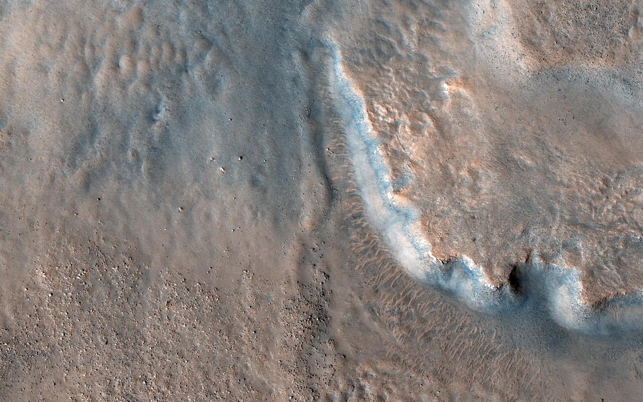 This image acquired by NASA's Mars Reconnaissance Orbiter on April 29, 2018, shows an impact crater approximately 23 kilometers across is home to fan-shaped deposits that extend from the rim and sit on the interior crater floor.  Thick beds with varying tone are exposed along the edge of the fan. Shallow valleys that carve into the smooth upland surfaces outside of the crater may provide clues regarding the formation of the deposits. Many boulder-sized blocks sit on the interior crater floor beyond the toe (distal edge) of the deposits.  This fan-hosting crater is located near the boundary between Tempe Terra and Acidalia Planitia in the Northern Hemisphere of Mars.   More information is available at https://photojournal.jpl.nasa.gov/catalog/PIA22592