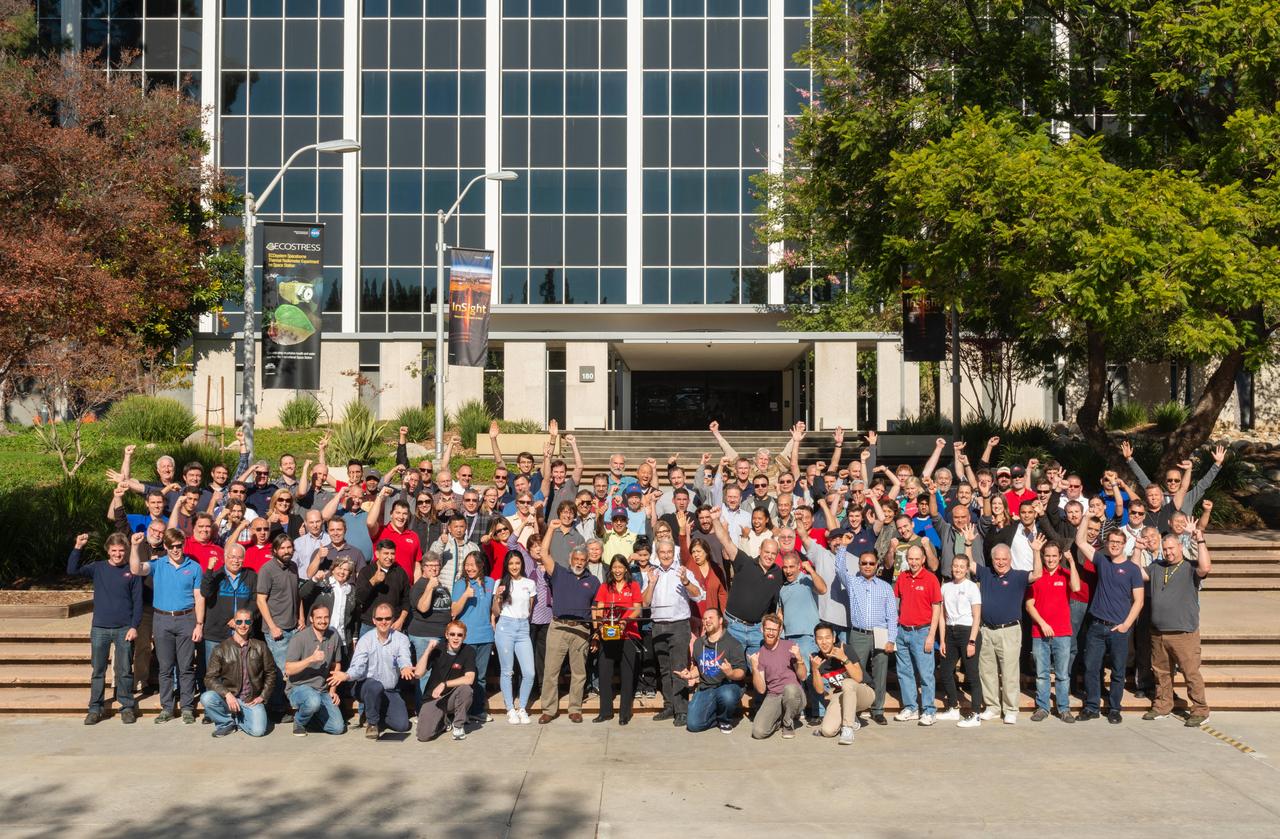 Morale was high as the Mars Helicopter team gathered for a group photo on Dec. 3, 2018, at NASA's Jet Propulsion Laboratory in Southern California. The helicopter, named Ingenuity, is a technology demonstration to test the first powered flight on another world. The helicopter will ride to Mars attached inside the belly of the Perseverance rover.  https://photojournal.jpl.nasa.gov/catalog/PIA22650