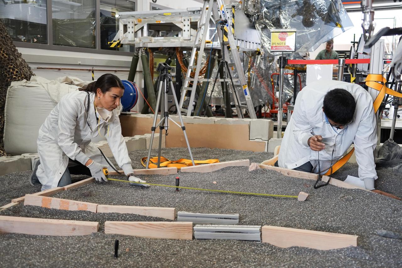 Engineers Marleen Sundgaard (left) and Pranay Mishra measure their test lander's "workspace" -- the terrain where scientists want to set InSight's instruments -- at NASA's Jet Propulsion Laboratory in Pasadena, California. Making sure each feature of the workspace on Mars is mimicked here on Earth allows for more reliable tests to be performed before actually setting down InSight's instruments. https://photojournal.jpl.nasa.gov/catalog/PIA22880