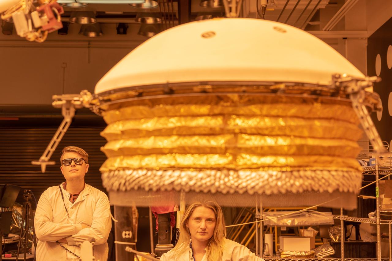 ForeSight, a fully functional, full-size model of NASA's InSight lander, practices deploying a model of the lander's Wind and Thermal Shield while engineers Phil Bailey (left) and Jaime Singer (center) look on. The Wind and Thermal Shield protects InSight's seismometer. This testing was done at NASA's Jet Propulsion Laboratory in Pasadena, California.  Bailey is wearing sunglasses to block the bright yellow lights in the test space, which mimic sunlight as it appears on Mars.  https://photojournal.jpl.nasa.gov/catalog/PIA22955