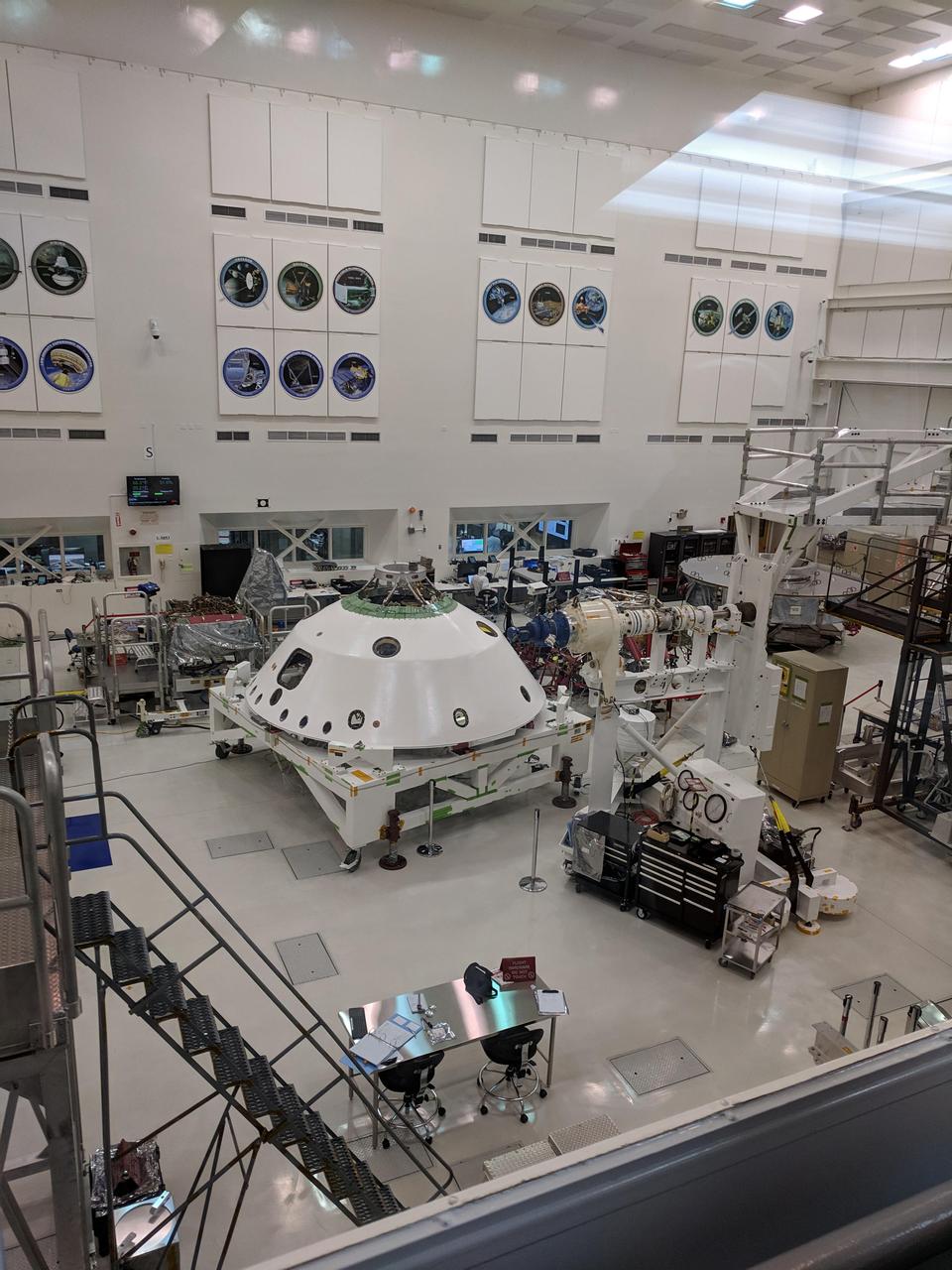 With the backshell that will help protect the Mars 2020 rover during its descent into the Martian atmosphere visible in the foreground, a technician on the project monitors the progress of Systems Test 1. Over two weeks in January 2019, 72 engineers and technicians assigned to the 2020 mission took over the High Bay 1 cleanroom in JPL's Spacecraft Assembly Facility to put the software and electrical systems aboard the mission's cruise, entry capsule, descent stage and rover through their paces.  https://photojournal.jpl.nasa.gov/catalog/PIA22966