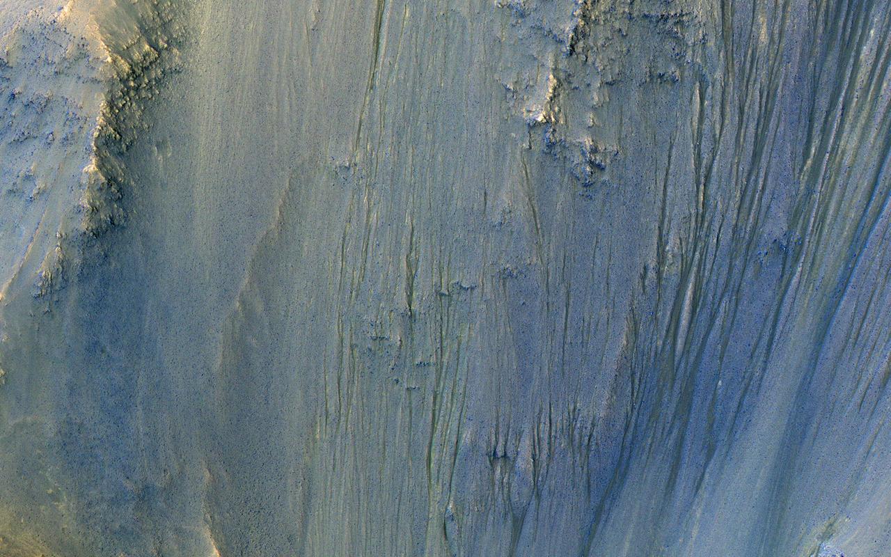 This image was acquired in Ius Chasma, a major section of the western portion of the giant Valles Marineris trough. We see a portion of a steep slope with gullies extending downhill (towards bottom of image). Many of the gully floors are dark, and in some places that dark material extends onto the fan-shaped deposits of the gullies. These dark features are candidates for recurring slope lineae (RSL), which are seasonal features that grow incrementally. The relation between RSL and gullies is not clear: does the RSL activity carve the gullies, or do they simply follow the gully topography created by other processes? Another closeup from this observation shows part of the floor of Ius Chasma, with layered bedrock draped by dunes. https://photojournal.jpl.nasa.gov/catalog/PIA23099