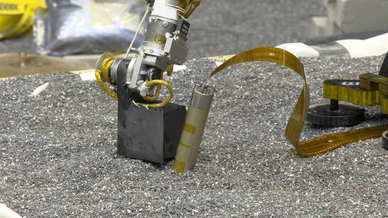In a JPL lab, a replica of NASA InSight's robotic arm presses with its scoop on crushed garnet near a replica of the spacecraft's self-hammering "mole." Engineers believe pressing like this on Martian soil may help the mole dig by increasing friction of the surrounding soil. https://photojournal.jpl.nasa.gov/catalog/PIA23276
