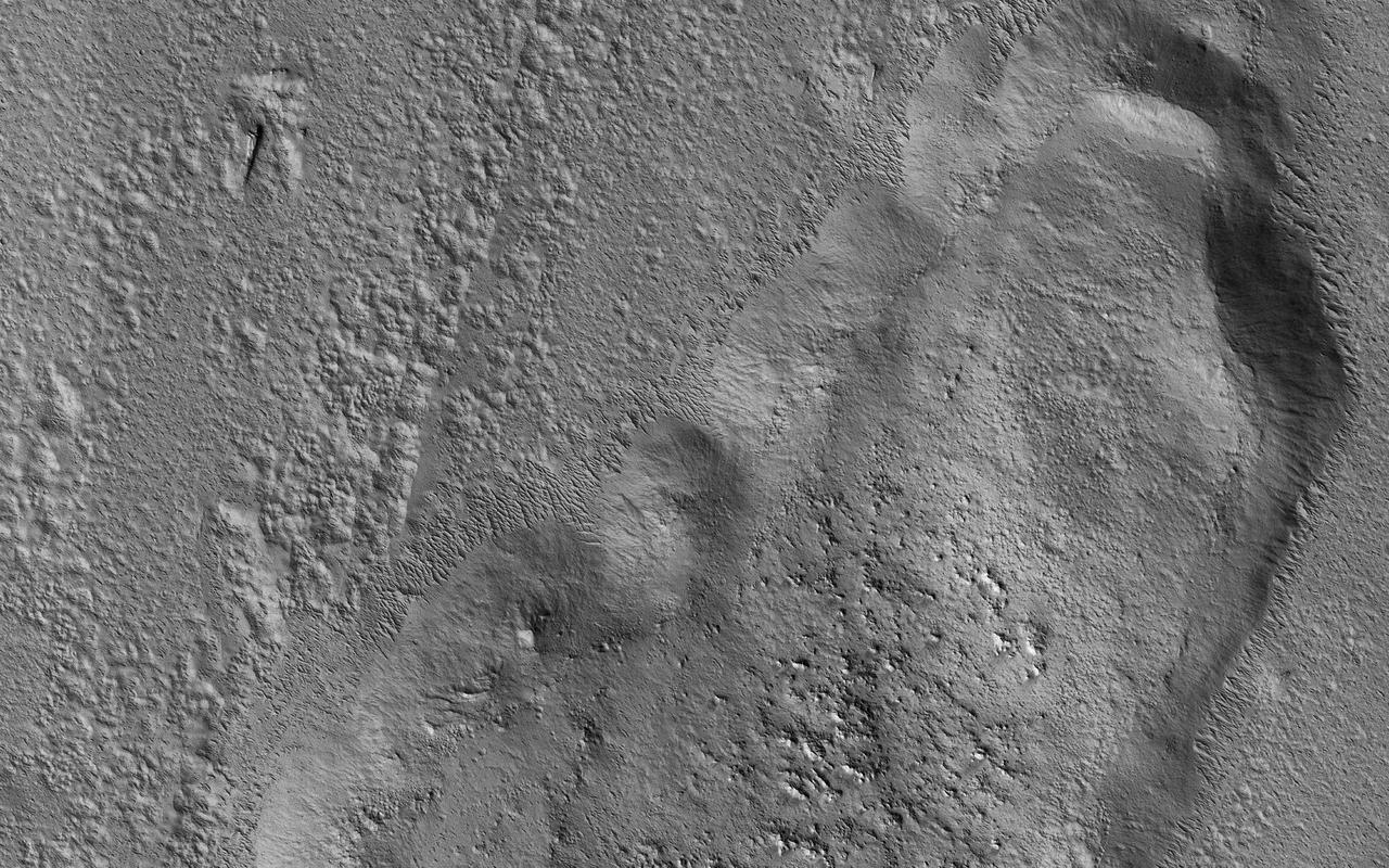 n this picture we can see a huge tongue-like form, which looks a like a mudflow with boulders on its surface. This "tongue" is only a small part of a larger deposit that completely surrounds Tooting Crater (not visible in this image). This is part of what is called an "ejecta blanket." The shape and form of the deposits in the ejecta blanket can tell us about the condition of the ground when the impact crater was formed. The presence of this tongue of ejecta is interpreted as a sign that the ground was frozen before impact. The force of the impact melted ice and mixed it with rock and dust as it was thrown away from the crater. It then settled to form these tongue-like lobes all around the crater. https://photojournal.jpl.nasa.gov/catalog/PIA23286