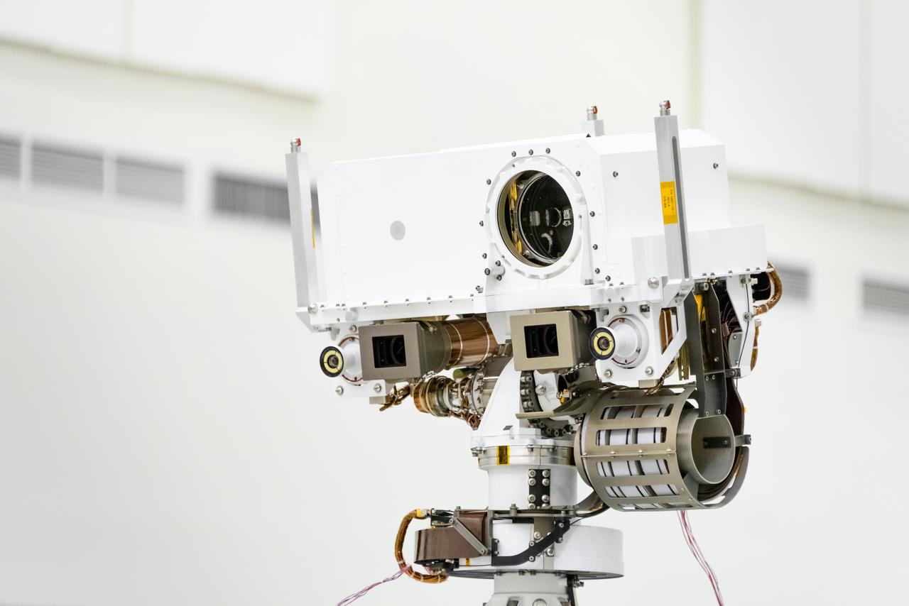This image, taken in the Spacecraft Assembly Facility's High Bay 1 at the Jet Propulsion Laboratory in Pasadena, California, on July 23, 2019, shows a close-up of the head of Mars 2020's remote sensing mast. The mast head contains the SuperCam instrument (its lens is in the large circular opening). In the gray boxes beneath mast head are the two Mastcam-Z imagers. On the exterior sides of those imagers are the rover's two navigation cameras.  https://photojournal.jpl.nasa.gov/catalog/PIA23316
